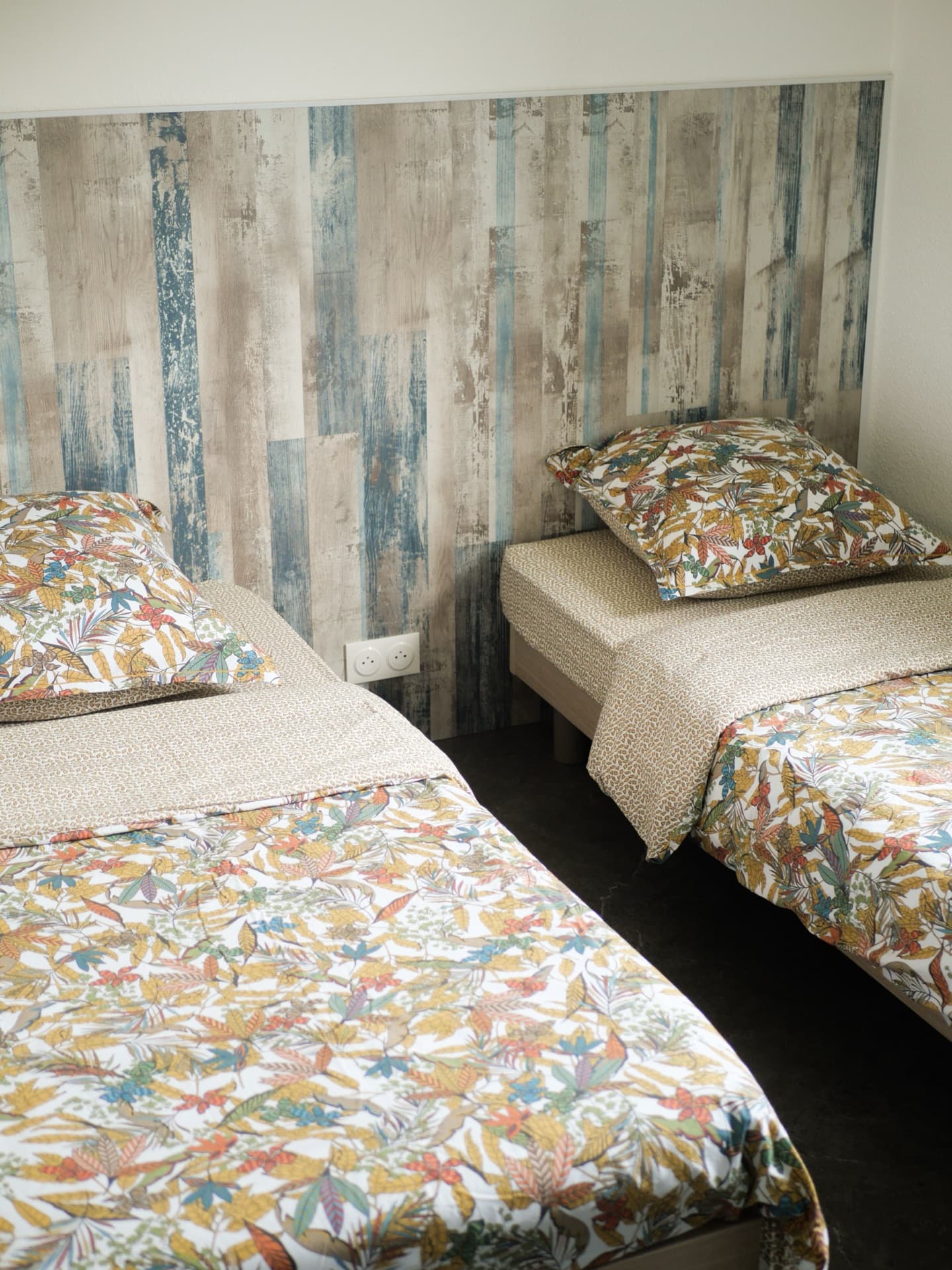 Chambre avec lits jumeaux, têtes de lit en bois flotté et parure feuilles