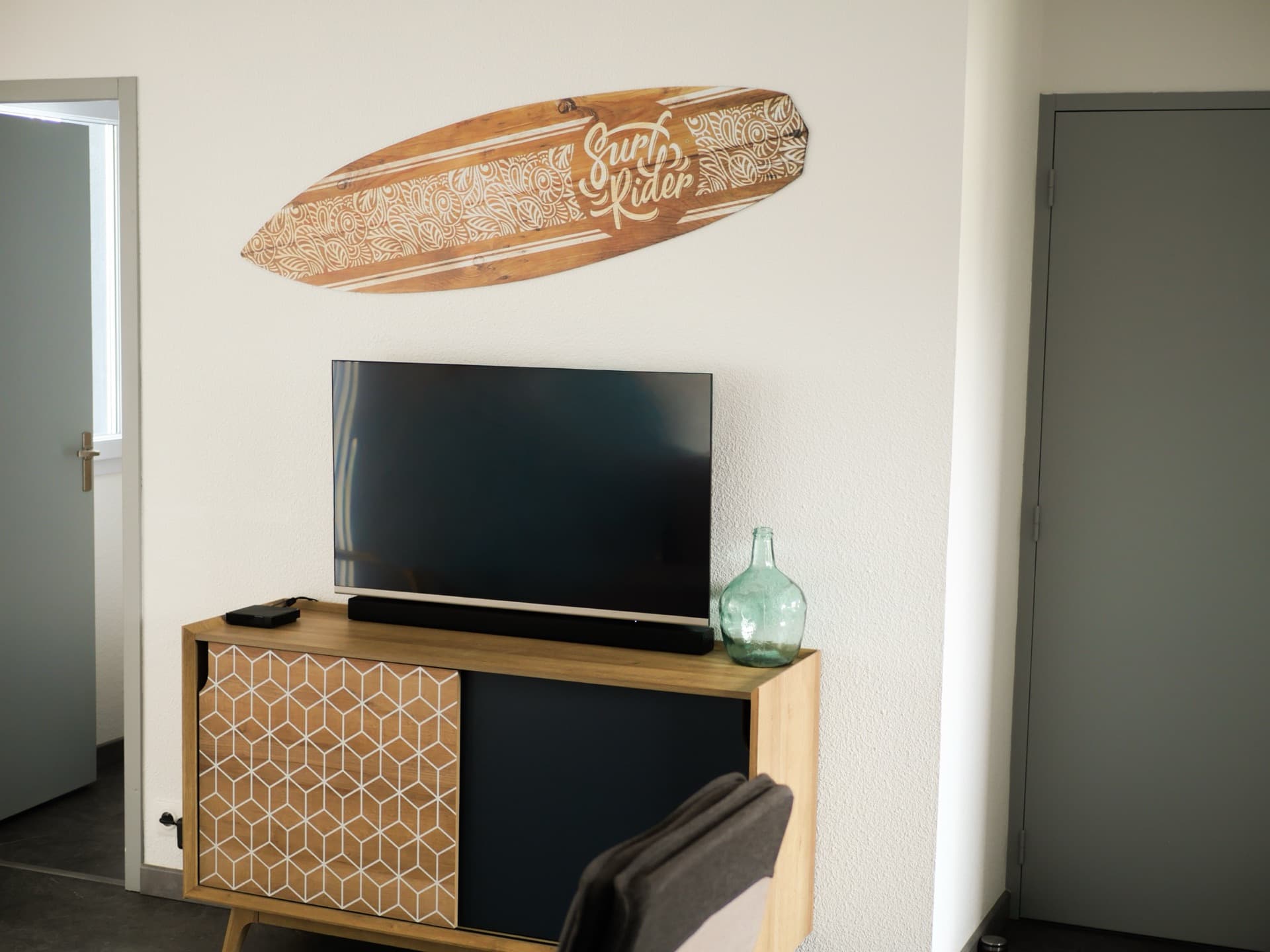 Coin salon avec télévision, fauteuil scandinave et porte vitrée vers la terrasse